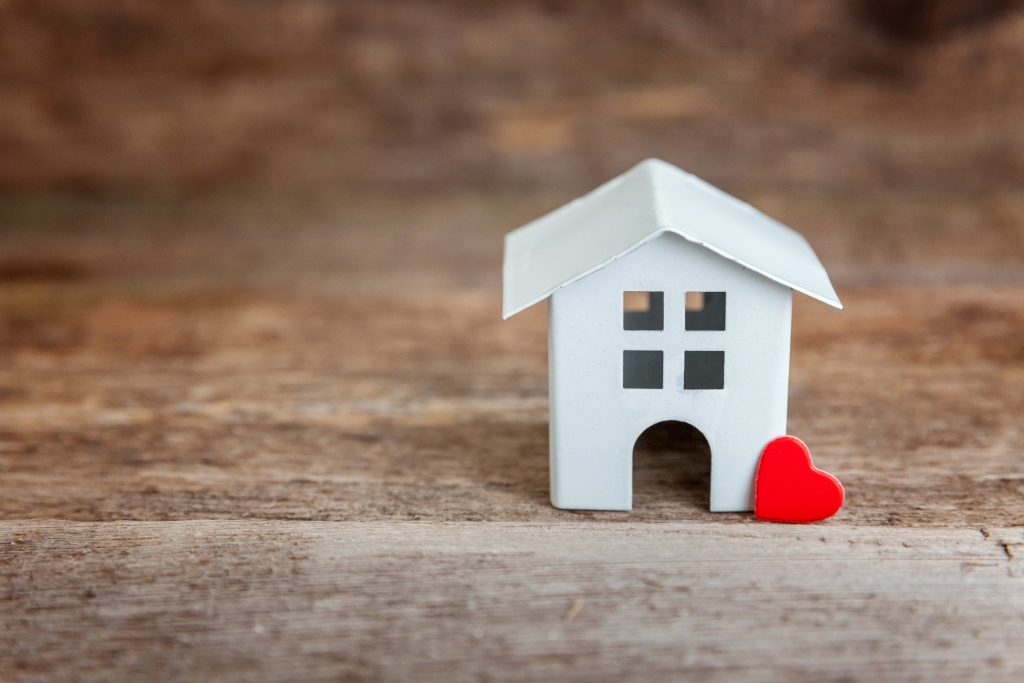 Miniature white toy house with red heart on a wooden table. Mortgage property insurance dream home concept